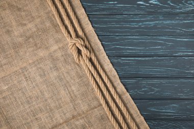 top view of knotted brown nautical rope on sackcloth on wooden background