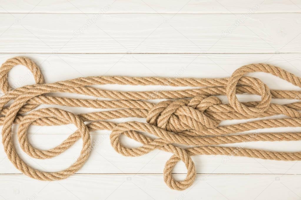 top view of brown nautical knotted ropes on white wooden surface