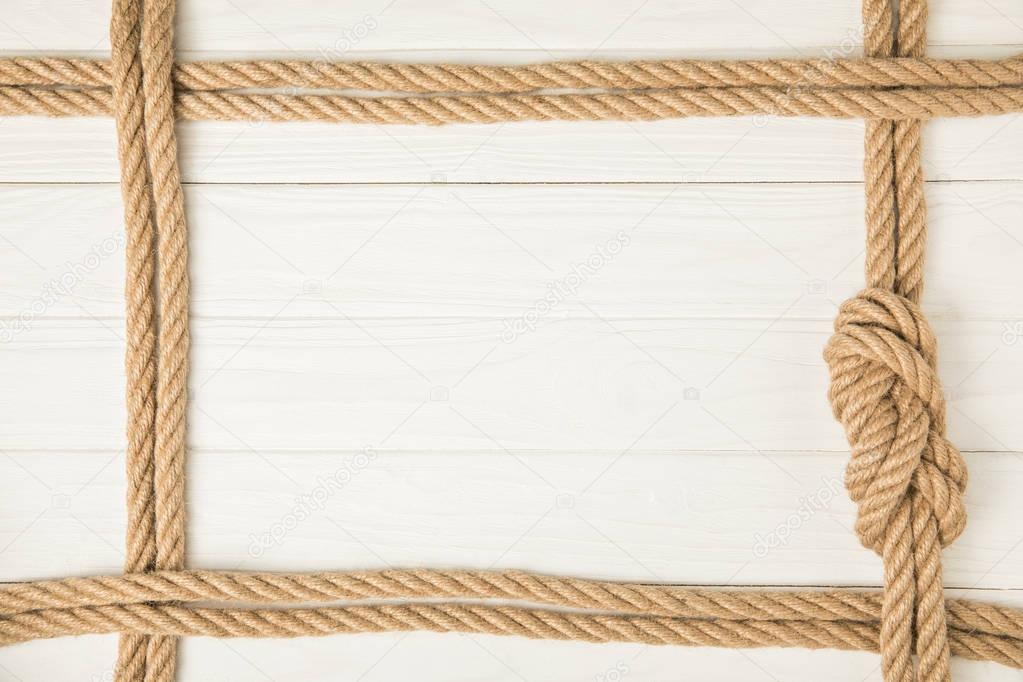 top view of frame made by brown nautical ropes with knot on white wooden background