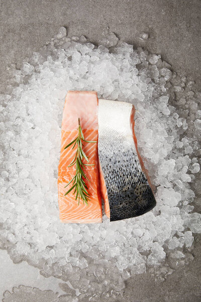 top view of sliced salmon fillet with rosemary on crushed ice and on concrete surface 
