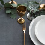 Close up view of rustic table arrangement with winecups, eucalyptus, vintage cutlery, candles in candle holders and empty plates