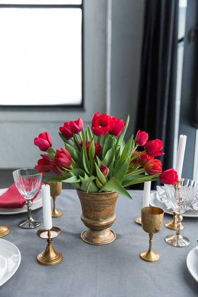 крупным планом букет красных тюльпанов на столешнице с устроенными старинными столовыми приборами и свечами
