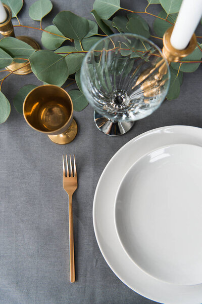 top view of rustic table setting with eucalyptus, old fashioned cutlery, candles in candle holder and empty plates
