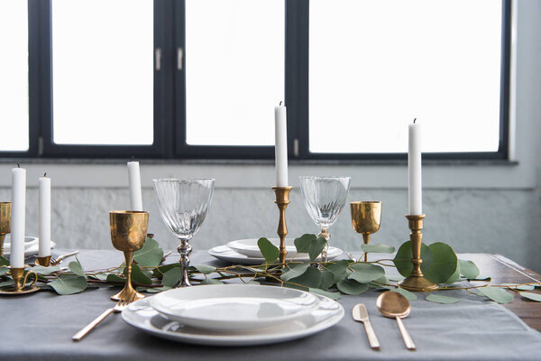 close up view of rustic table arrangement with eucalyptus, tarnished cutlery, candles in candle holders and empty plates