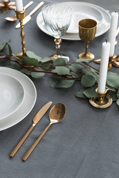 close up view of rustic table arrangement with eucalyptus, vintage cutlery, candles in candle holders and empty plates