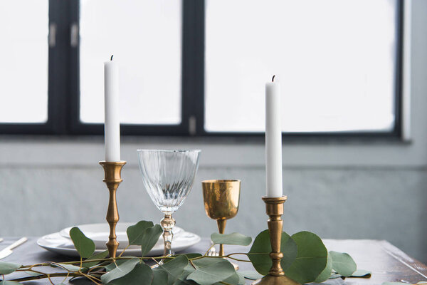 close up view of rustic table arrangement with wine glasses, eucalyptus, candles in vintage candle holders and empty plates