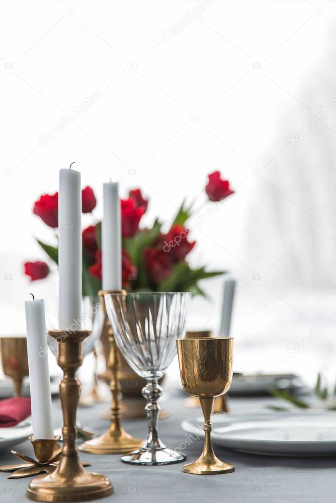 selective focus of candles in vintage candle holders, bouquet of red tulips and arranged empty plates on tabletop