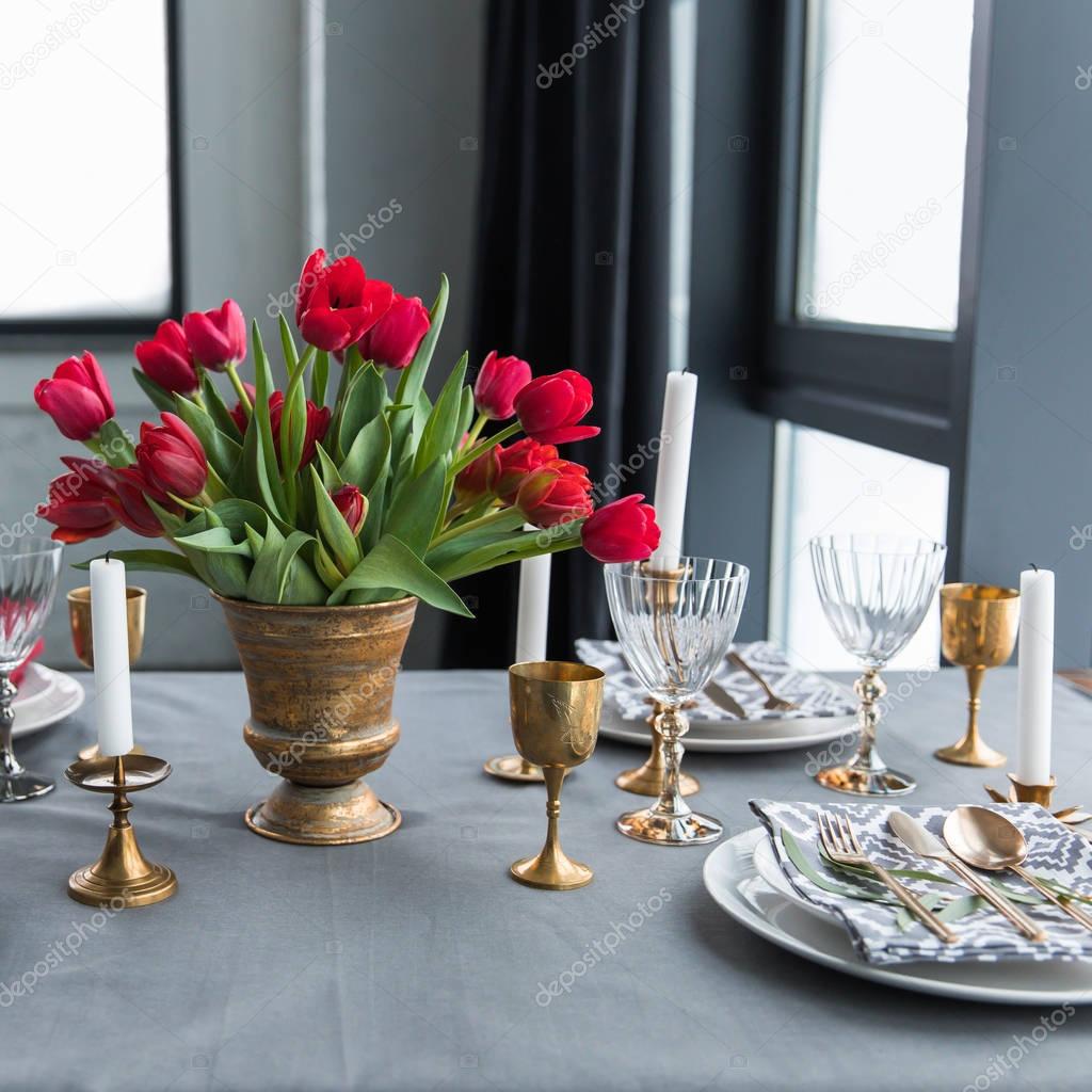 close up view of bouquet of red tulips on tabletop with arranged vintage cutlery and candles