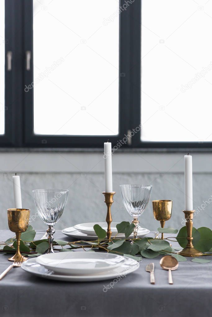 close up view of rustic table setting with eucalyptus, vintage tarnished cutlery, candles in candle holders and empty plates