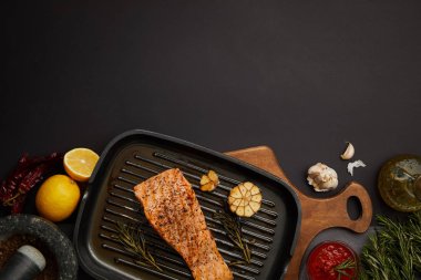 ahşap kesme tahtası, sos, malzemeler ve çatal bıçak takımı siyah masa üzerinde görücü usulü ızgara somon Steak Üstten Görünüm