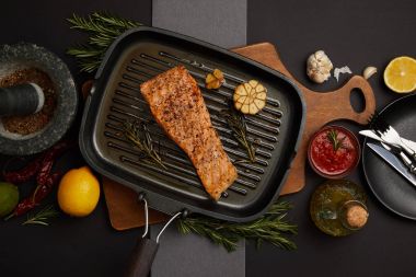 ahşap kesme tahtası, sos, malzemeler ve çatal bıçak takımı siyah masa üzerinde görücü usulü ızgara somon Steak Üstten Görünüm