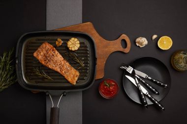ahşap kesme tahtası, sos ve çatal bıçak takımı siyah masa üzerinde görücü usulü ızgara somon Steak Üstten Görünüm