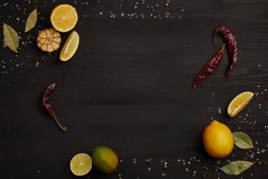 limon ve kireç parçaları, baharat, biber ve defne yaprağı üzerinde siyah masa üstü düz lay
