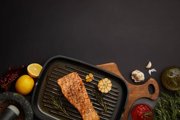 木製のまな板 ソース 食材と黒いテーブルの上の食器整理されたグリル サーモン ステーキのトップ ビュー — ストック写真