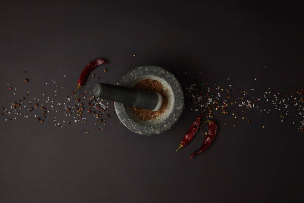 flat lay with mortar, pestle, spices and chili peppers on black tabletop