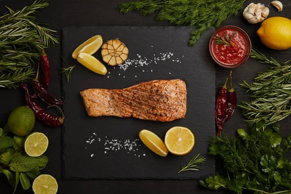 siyah yüzey üzerinde ızgara somon Steak adet limon ve çevresinde düzenlenmiş malzemeler ile Üstten Görünüm