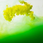 Vista de perto de mistura de tintas verdes e amarelas salpicos em água isolada em cinza