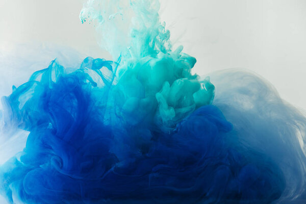 close up view of mixing of blue and turquoise paints splashes in water isolated on gray