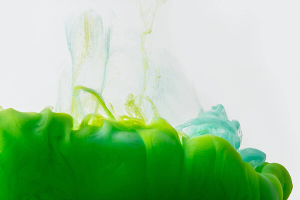 close up view of mixing of green and bright turquoise paints splashes in water isolated on gray