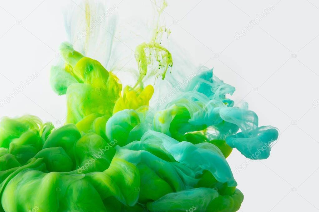 Close up view of mixing of green, yellow and bright turquoise inks splashes in water isolated on gray