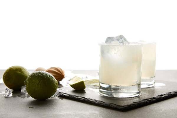 close up view of refreshing sour alcohol cocktails with lime and ice on tabletop on white