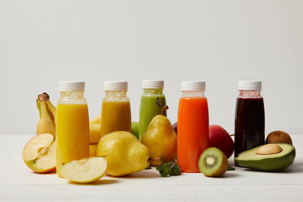 fresh fruits and detox smoothies in bottles on white wooden surface   