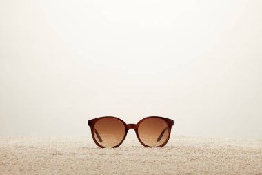 close up view of sunglasses on sand on grey background clipart