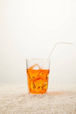 close up view of refreshing cocktail with ice and straw on sand on grey background clipart