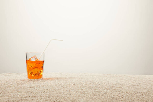 close up view of refreshing cocktail with ice and straw on sand on grey background