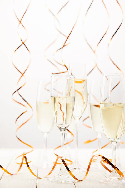 Champagne glasses with golden streamers on white wooden table, holiday concept