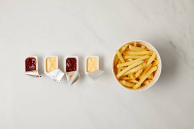 top view of french fries in bowl with containers of sauces in row on white clipart