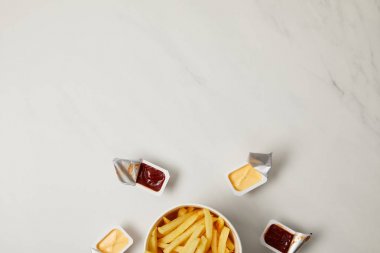 top view of french fries in bowl surrounded with containers of sauces on white clipart