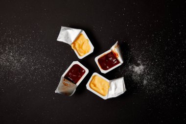 top view of plastic containers with sauces on black surface spilled with salt clipart
