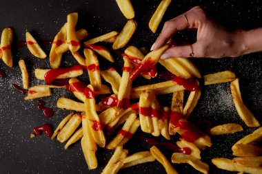top view of woman taking french fries poured with ketchup on black tabletop clipart
