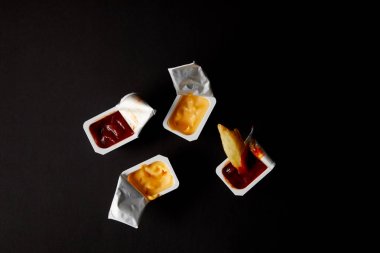 top view of plastic containers with sauces and poured french fry isolated on black clipart