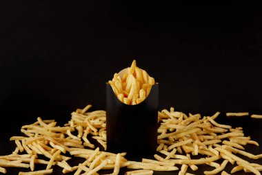close-up shot of tasty french fries in black box surrounded with messy fries on tabletop isolated on black clipart