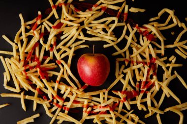 top view of red apple surrounded with french fries poured with ketchup isolated on black clipart