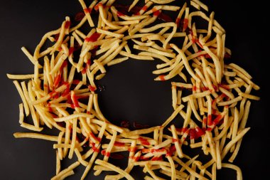 top view of french fries in shape of circle poured with ketchup isolated on black