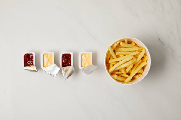top view of french fries in bowl with containers of sauces in row on white