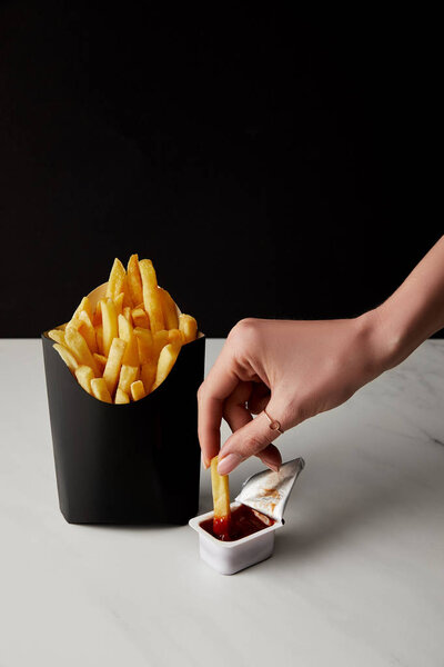 cropped shot of woman pouring french fry into ketchup isolated on black