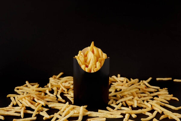 close-up shot of tasty french fries in black box surrounded with messy fries on tabletop isolated on black