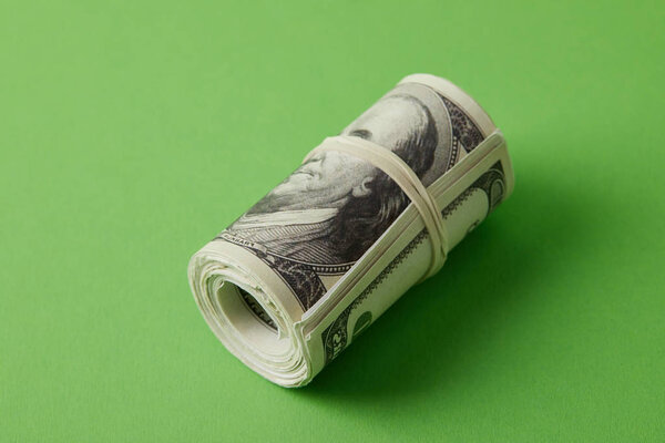 roll of dollars tied with rubber band on green surface
