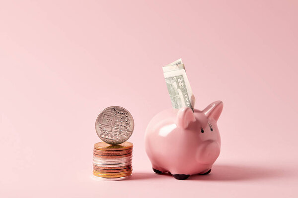 stack of bitcoins and piggy bank with cash on pink