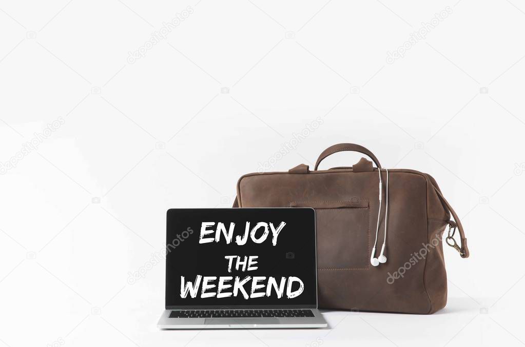 laptop with Enjoy the weekend lettering on screen and stylish bag with earphones, isolated on white