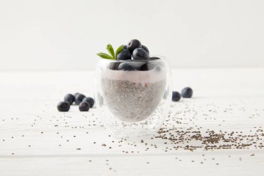 close up view of sweet chia seed pudding with blueberries and mint on white wooden surface clipart