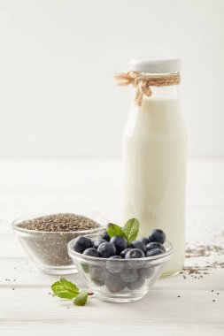 şişe süt, yaban mersini ve üzerinde beyaz ahşap masa üstü chia puding yapmak için chia tohum görünümünü kapat
