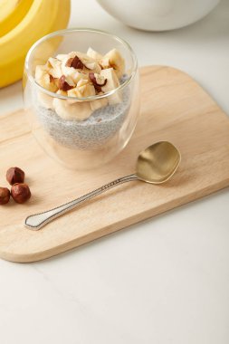 close up view of tasty chia seed pudding with pieces of banana and hazelnuts on wooden cutting board with spoon clipart