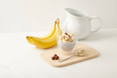 close up view of tasty chia seed pudding with bananas and hazelnuts on white tabletop clipart