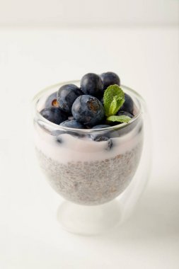 close up view of chia seed pudding with blueberries and mint on white surface clipart