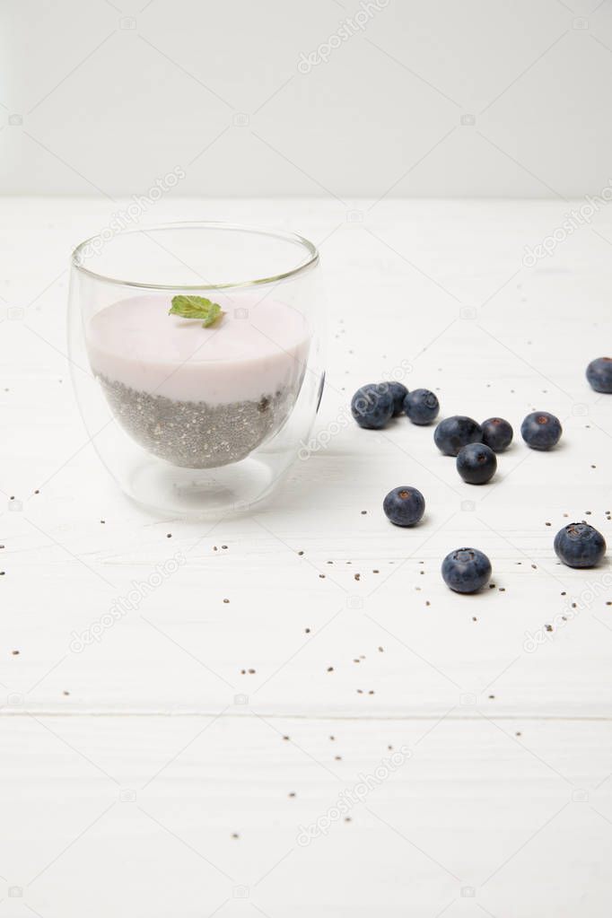 close up view of chia seed pudding with mint leaves and fresh blueberries on white tabletop